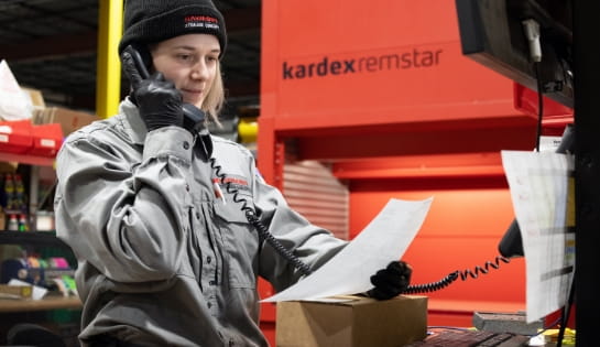 RSCI parts specialist in parts cage taking a phone order with sheet of paper in her hand. Kardex Remstar AS/RS in the background.