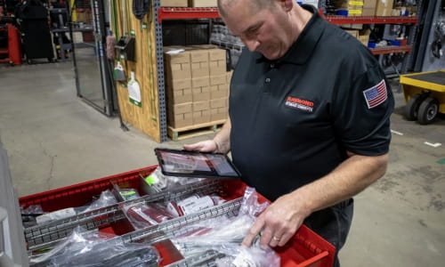 RSCI parts specialist counting inventory for a parts consignment customer in a warehouse. He's holding a tablet.