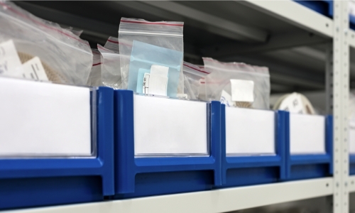 Multiple blue labeled bins with tiny bags of parts on cabinet shelf.