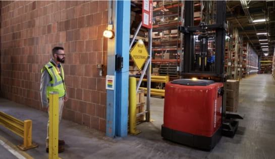 Warehouse pedestrian in safety vest stopped at doorway as an automated forklift drives by.