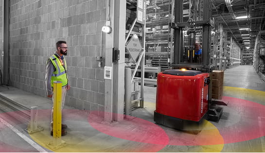 Pedestrian warehouse worker walking towards passageway in warehouse at the same time as a forklift. The radial circles on the floor to demonstrate sensing technology.
