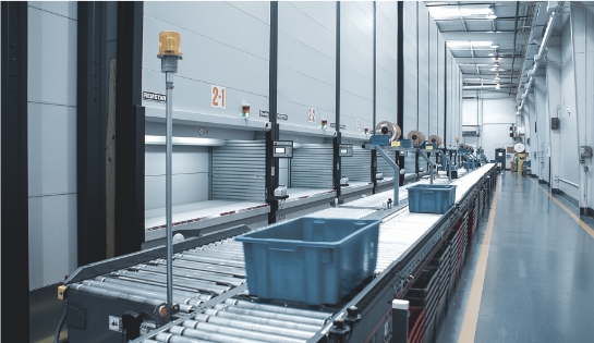 Totes rolling down a conveyor for a picker. In front of multiple VLM systems.