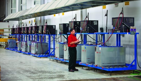 RSC energy specialist with a clipboard reviewing a line of power systems on a warehouse wall.