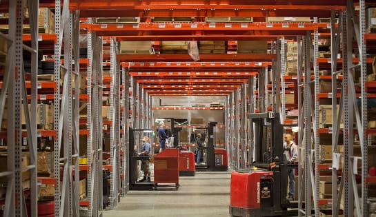 Warehouse aisles with Raymond forklifts moving between gathering orders.