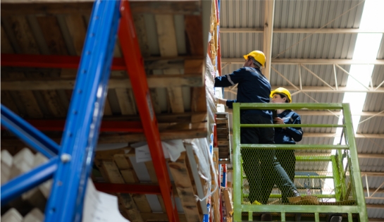 Two workers with jumpsuits and hard hats in a scissor lift installing racking.