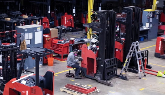 Technician working in warehouse shop refurbishing used forklifts.