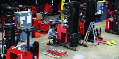 Technician working in warehouse shop refurbishing used forklifts.