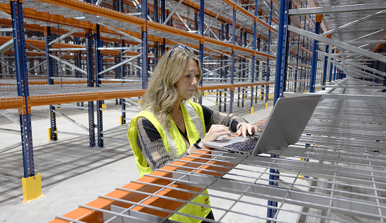 RSC account manager looking at her laptop sitting on a wire deck in a warehouse racking aisle.