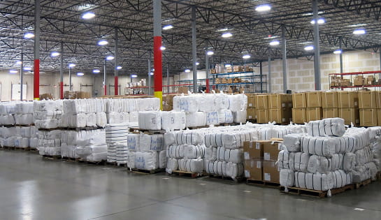 A before view of Standard Textile's storage area. Warehouse floor space is covered in textile bales and carton pallets stacked on the floor.