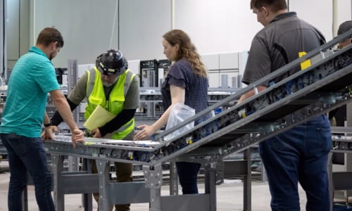 Man in hard hat and safety vest demonstrating progress on a conveyor install to three RSCI employeers—project manager and design engineers.