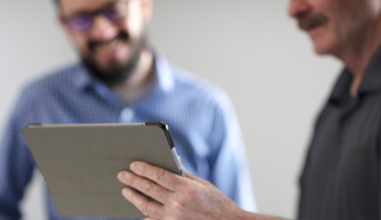 A person holding a tablet with a man in blue in the background.