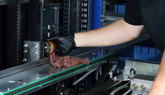 Gloved hand cleaning a wheel with a rag inside an AS/RS system.