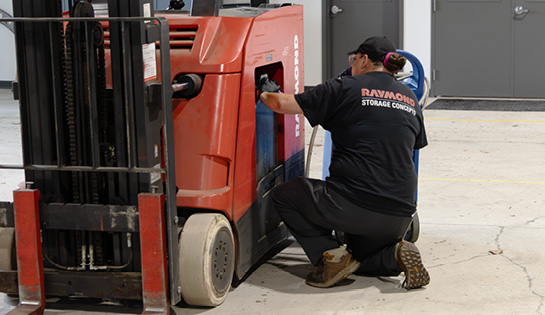 RSC female technician bent down to water a lead-acid battery in a Raymond counterbalanced truck with watering gun.