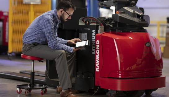 RSC rep holding a tablet review iBATTERY dashboard next to a Raymond forklift and battery.