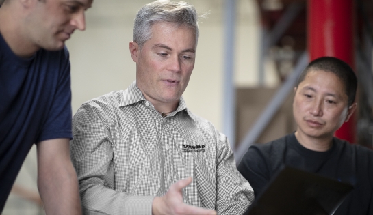 RSC employee in the middle of two men talking and showing the two men something.