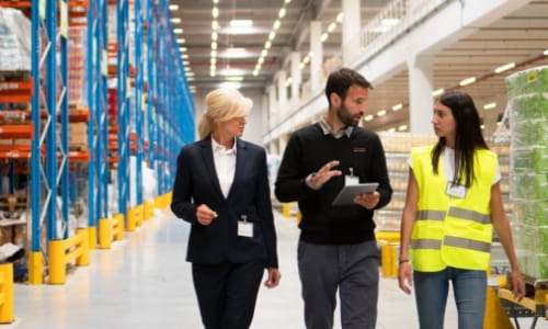 Three people walking and talking in a warehouse. One female operations manager, one RSC male account manager and one female warehouse worker in safety vest.