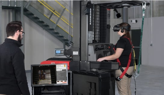 Forklift operator trainee on forklift with VR headset on practicing operations. Trainer to the side viewing monitor to trainees VR training progress.