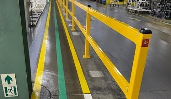 Yellow safety guardrail placed between a pedestrian walkway and active warehouse.