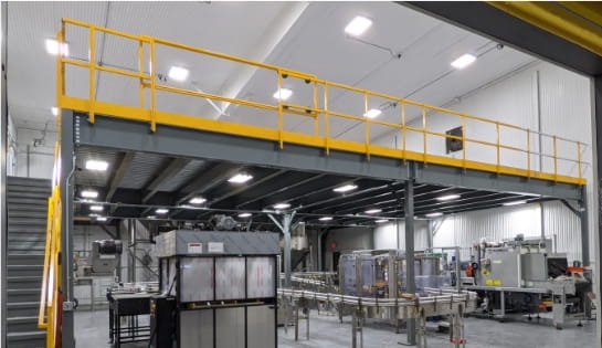 Gray mezzanine over manufacturing machinery in a warehouse.