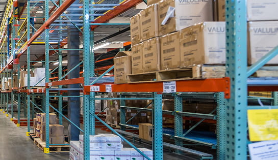 Warehouse aisle of boxes and cartons. On the horizontal bar of the rack is labels to help with inventory management