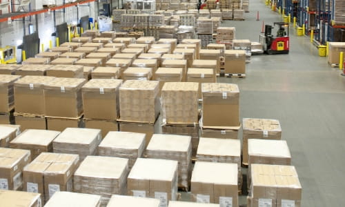 Staging area in a warehouse with many rows of pallets. A forklift pulling pallets to place in the racks.